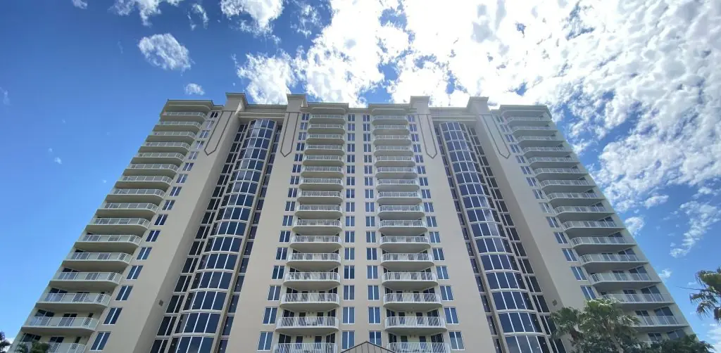 One Beach Club Drive condominium tower seen from grade, stacked balconies and window wall against a bright coastal sky, Miramar Beach, Florida.