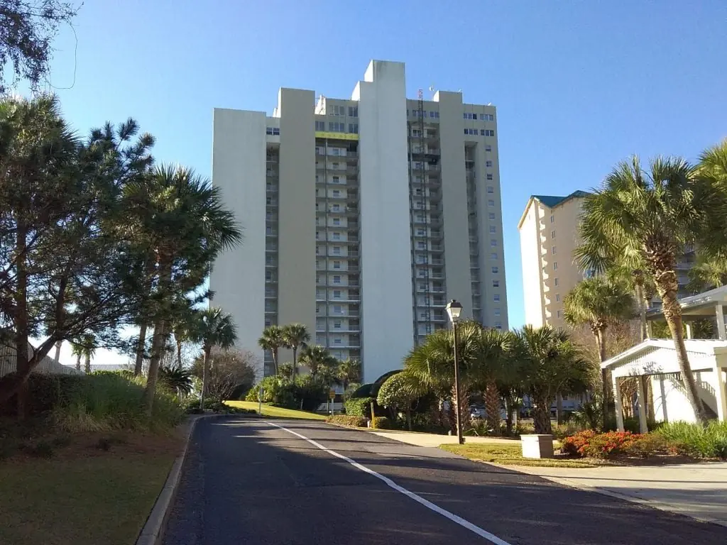 Gulf Side at Hidden Dunes condominium tower rising above the tree line under clear sky, Miramar Beach, Florida.